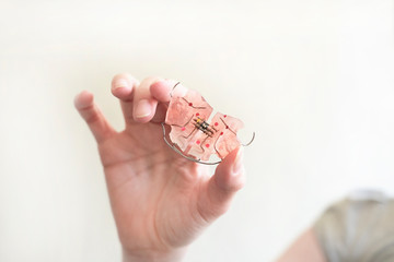 A dental plate in hand that helps align growing teeth against an white background. An orthodontic trainer. A way to have a beautiful smile and healthy teeth.