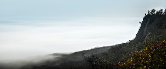 Banner, web page or cover template of Alone man standing on the top of the rocks over the valley full of mist - thinking, sad, alone, depression concept photo. Copy space and panoramic ratio © kovop58