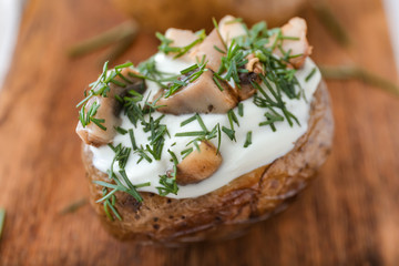Tasty baked potato with sour cream and mushrooms on board, closeup