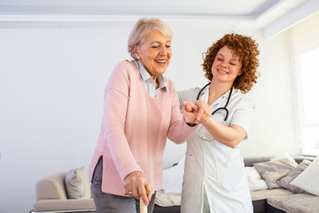 Smiling nurse helping senior lady to walk around the nursing home. Portrait of happy female caregiver and senior woman walking together at home. Professional caregiver taking care of elderly woman.