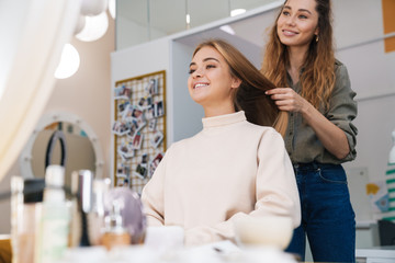 Blonde girl indoors in beauty salon with hairdresser.