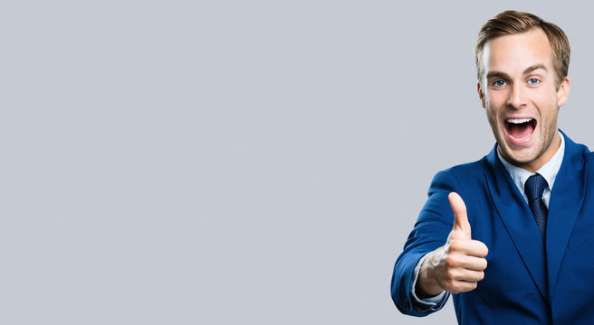 Portrait of very happy excited businessman showing thumbs up gesture, over grey background. Business success concept. Blank copy space area for advertisiment, slogan or text.