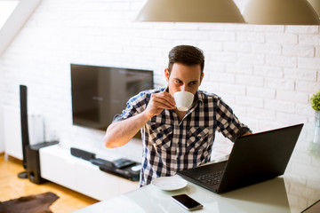 Young man sitting on kitchen desk at home and using laptop and drinking coffee