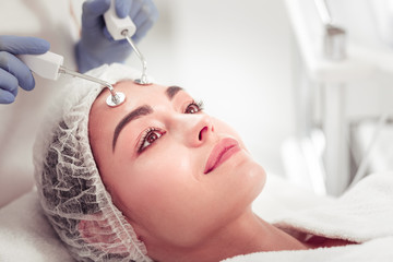 Dark-eyed woman feeling relaxed enjoying apparatus face cleansing