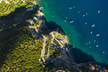 Aerial shot to the sea with boats and rocky green shore. Serpentine road along the mountains. South Italy. Beaautiful landscape. View from above.