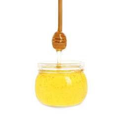 Honey dripping from dipper in jar on white background