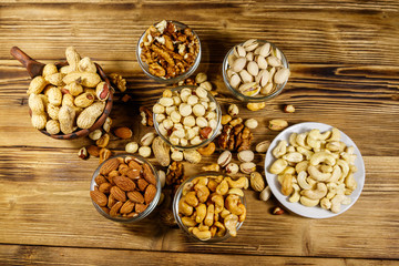 Assortment of nuts on wooden table. Almond, hazelnut, pistachio, peanut, walnut and cashew in small bowls. Top view. Healthy eating concept