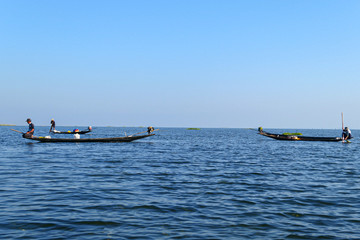 Aisan fisherman on the wooden boat on the lake. Men fishing on the blue river.