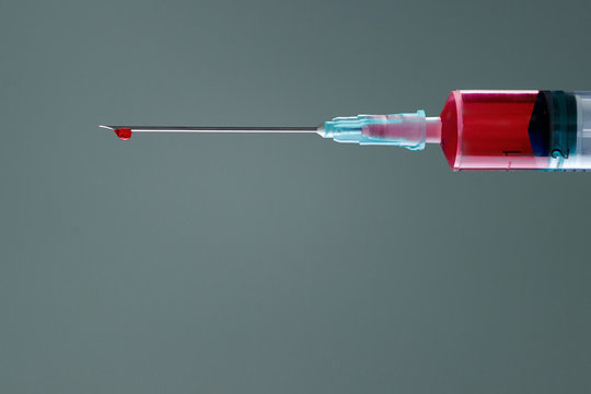 The end of the syringe with a needle filled with liquid, on a neutral background.