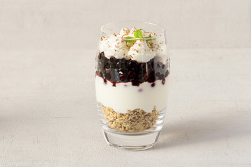 Layered oatmeal breakfast in a glass with crunchy nuts and oats, yogurt, blueberries, and mint. Isolated, copy space. Healthy vegetarian breakfast, dessert or snack.