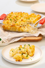 Macaroni and cheese in transparent dish on cotton towel on the table. There is a spoon inside it. One portion in the plate. Homemade vegetarian lunch or dinner. Close up. 