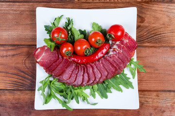 Dried-smoked pork neck, herbs, tomatoes on dish, top view