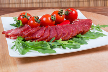 Dried-smoked pork neck among the greens and tomatoes closeup