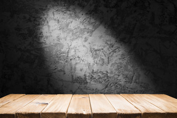 Old wood table with blurred concrete block wall in dark room background.