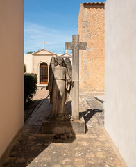 großer Engel neben einem Steinkreuz auf einem Friedhof in Spanien
