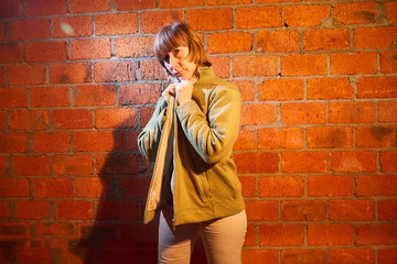 A middle-aged woman poses showing clothes near red brick wall. An inept model in an inept shoot