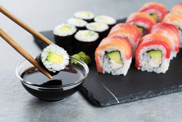 Sushi maki with avocado, sushi philadelphia, soy sauce and wasabi. Chopsticks taking portion of sushi roll. © vitals