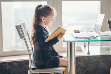 School girl  is studying online. Home schooling. Distance education. Little girl is reading book.