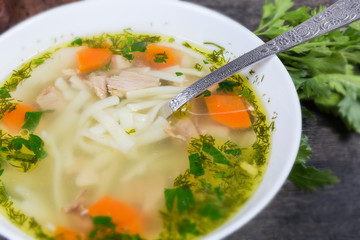 Chicken noodle soup in bowl with spoon, fragment close-up