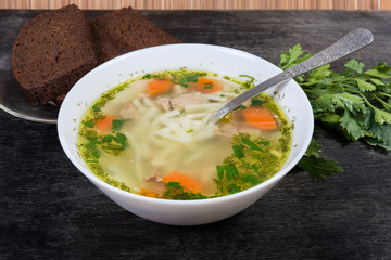 Chicken noodle soup in bowl against the bread and greens