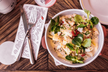 pasta with sauce, cheese and basil in a white dish on a wooden table in a restaurant, a rowl knife and fork
