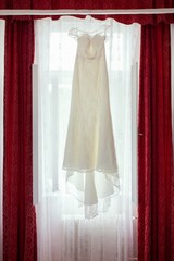 Wedding dress with crystals and pearls hangs
Elegant wedding dress with a train hanging on window. Wedding morning