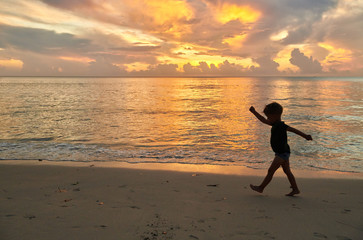 Fototapeta na wymiar Toddler boy walking on beach at sunset