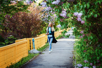 Fototapeta na wymiar Attractive woman is walking through the lilac alley in spring. Student girl is spending time in the countryside. 