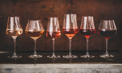 Various shades of Rose wine in stemmed glasses placed in line from light to dark colour on concrete...