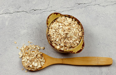 Oat flakes in bowl and wooden spoon on a light gray background. Top view, flat lay