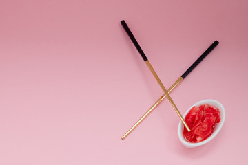 Marinated ginger and chopsticks with black handles, folded cross on a pink background. Flat lay with copy space, selective focus. Japanese food. Horizontal orientation.