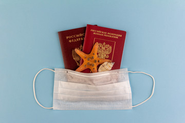 two Russian passports, a starfish and a seashell under a disposable medical mask on a blue background close-up view from above, the concept of self-isolation during the coronavirus COVID-19 pandemic