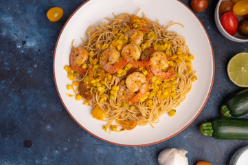 Stir fry with shrimp and pasta. On a blue texture with ingredients.