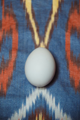 Single white egg on red and white hand woven atlas cloth. Easter decorations and preparations for the holiday. Natural, organic and healthy food.