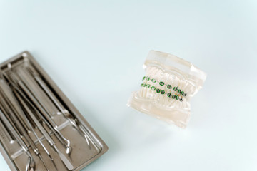 Stainless steel medical tray with dental instruments: mirror, probe, scrapers. Model of the jaw with braces on a blue background next to dental instruments