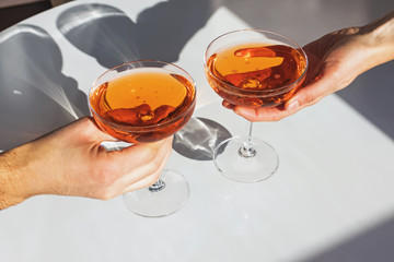 Close up view of man and woman hands holding glasses with cocktail of orange color