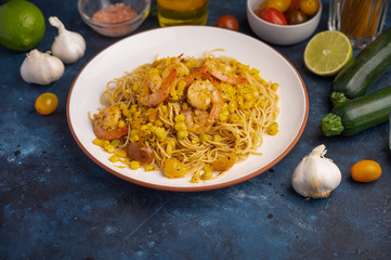 Stir fry with shrimp and pasta. On a blue texture with ingredients.