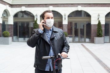 man in a medical mask on a background of a modern building on electric scooter, coronavirus, illness, infection, quarantine, medical mask