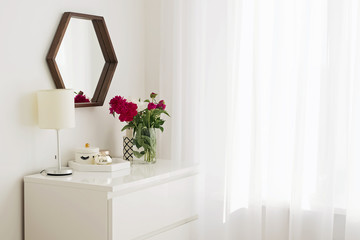 A part of modern bedroom in white colors with bouquet of peonies