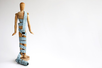 Isolated wood adjustable mannequin holding and wrapped in a blue tape measure for a weight loss and plastic surgery beauty concept