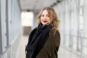 Closeup portrait of a happy young woman smiling. Stylish fashion portrait woman. Posing in the city. Beautiful girl in autumn green coat and black scarf poses in an overhead pedestrian crossing.