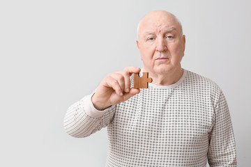 Elderly man suffering from mental disability with puzzle piece on grey background