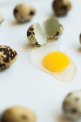 Small quail eggs on white background, one broken, with yellow yolk, eggshell and protein. Easter concept. Unusual paschal photo.