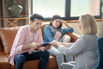 Dark-haired tall man sitting next to his girlfriend and passing documents to a blonde woman