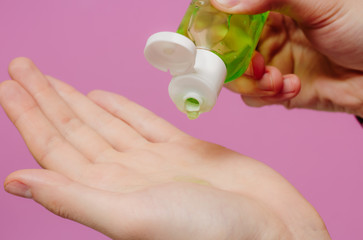 The guy treats his hands with an antibacterial sanitizer. Pink background. Medical content