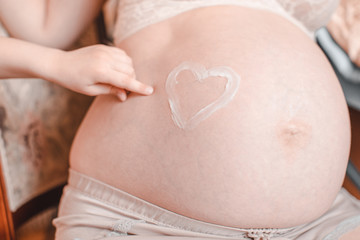 Heart shape painted with creme on belly of pregnant woman. Closeup of pregnant woman holding her belly