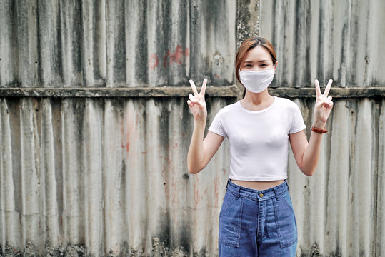 Asian woman wearing mask. Young Asian lady wearing face mask for protecting Coronavirus Covid 19 with victory gesture. Coronavirus Covid 19 outbreak pandemic.