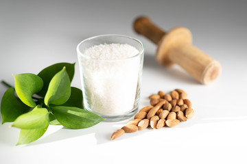 coconut flakes in a glass and sprinkled almonds on a white background, with a green leaf of a plant.