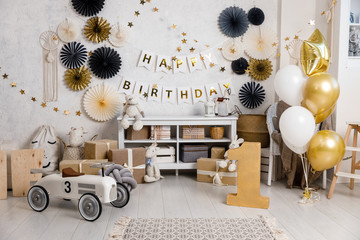 Birthday decorations with balloons, gifts, toys, garlands and candy for yearling, little baby party, celebration on a white wall background. Black and gold Decor elements.