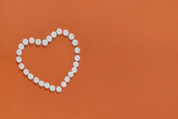 The heart made of tablets and pills on Orange background